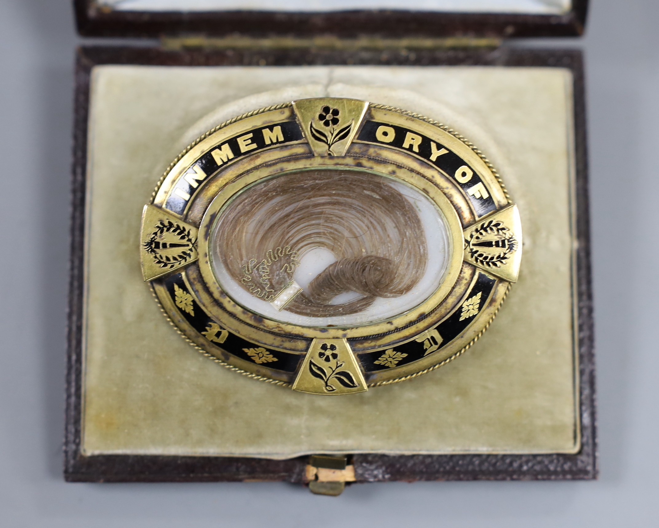 A Victorian yellow metal and black enamel oval memorial brooch, in original box, with plaited hair and inscribed verso 'Peter Dixon Died 14th July 1878 aged 23' with photograph, width 58mm, gross weight 27.9 grams.